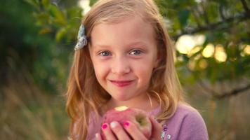en söt liten flicka som äter ett nytt äpple från ett träd och ler