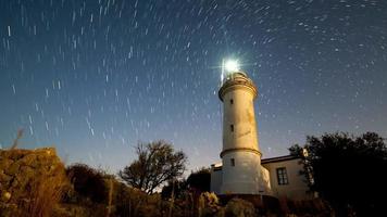 4K. Timelapse of beautiful night landscape with lighthouse with rotating starry sky on a background