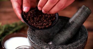 Black peppercorns being put into a mortar and pestle