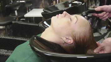 professionell frisör tvätta hår av blond ung flicka i skönhetssalong i speciella bad. hårvård video
