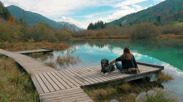 A red haird gril sits on a dock with her dog video