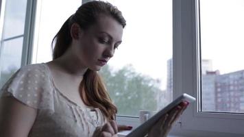 fille assise près de la fenêtre et utilisant une tablette numérique. fermer.