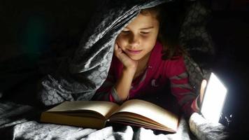 barn tonårig läsande flicka läser bokhund på natten med ficklampa som ligger under en filt
