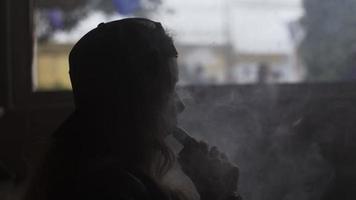 Silhouette girl in cap exhalation steam circle from electronic cigarette. Smoker video