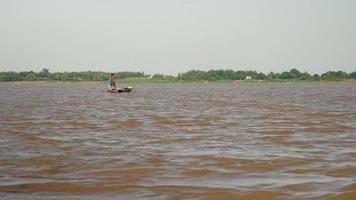 uomo che rema la sua piccola barca sul fiume mentre tira una rete da pesca attraverso l'acqua dietro video