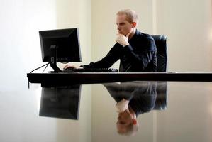 Hombre caucásico blanco sentado en la computadora detrás de un escritorio de cristal foto