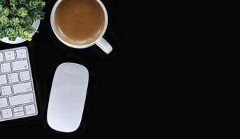 Vista superior del espacio de trabajo con un teclado, mouse y café sobre una mesa negra foto