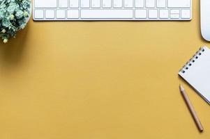 Top view of a yellow desk with a keyboard and notepad photo