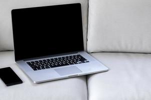 Laptop mockup with a smartphone on a sofa photo