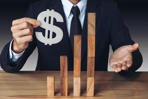 Businessman holding a dollar sign with stacked wooden blocks photo