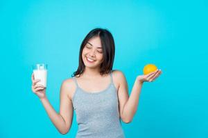 joven mujer asiática sosteniendo un vaso de leche y una naranja foto