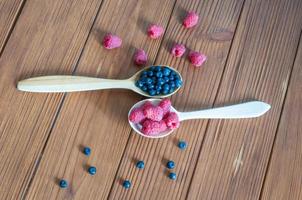 Raspberries and blueberries in spoons on wooden background. Healthy eating