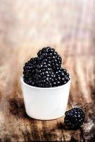 Fresh Blackberries in a white bowl on  wooden table closeup photo
