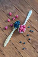 Fresh blueberries and raspberries in wooden spoon. Dark wood background