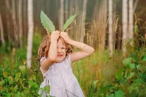 child girl playing with green leaves in summer forest