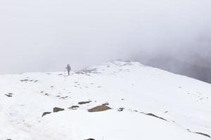 Woman backpacker tourist hiking ascending snow mountain covered fog.