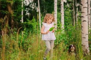 child girl playing with green leaves in summer forest
