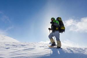 Hombre mochilero caminando en las montañas de invierno en un día soleado foto