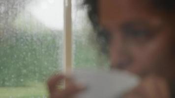kvinna som dricker kaffe hemma med regn på fönstret video