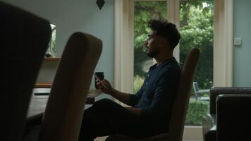 Joven enviando mensajes de texto por teléfono trabajando desde casa video
