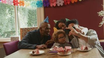Famille multiethnique célébrant l'anniversaire du garçon en prenant une photo au téléphone video