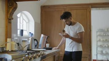 jonge man telefoon controleren tijdens het maken van koffie