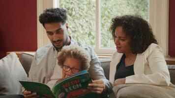 Young boy reading book with parents at home video