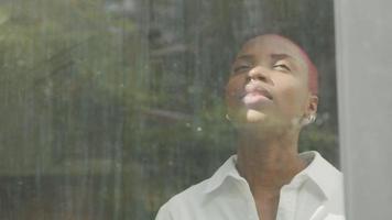 Young woman with shaved hair looking through window video