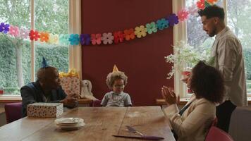 Boy blowing out candles on cake with family singing happy birthday video