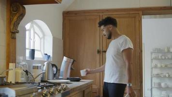 jonge man koffie maken in de keuken en telefoon kijken video