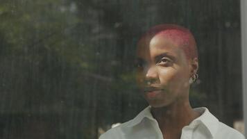 Mujer joven con el pelo rapado mirando por la ventana video