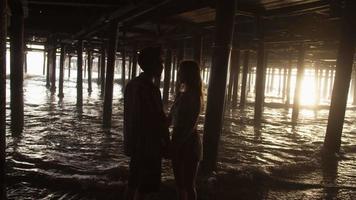 Cámara lenta de la joven pareja cogidos de la mano bajo el muelle video