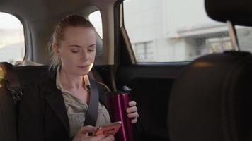 Slow motion of woman in taxi using phone and drinking coffee