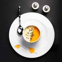 Pumpkin soup with cream and seeds in white bowl