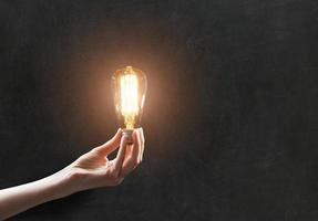 hand holding Light bulb on blackboard background