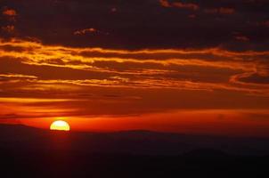 puesta de sol sobre la montaña con cielo rojo y nube dorada foto
