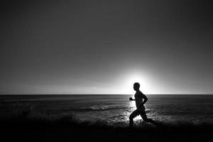 Silhouette of jogger along ocean horizon at sunset photo