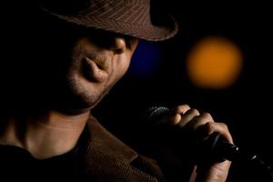 African American male singer wearing a fedora at microphone