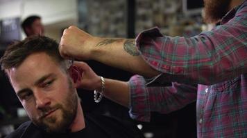 Peluquero masculino dando corte de pelo al cliente en la tienda video