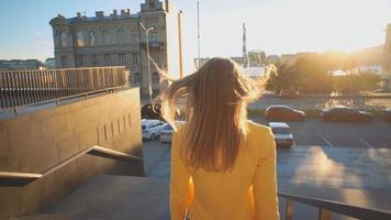junges schönes Mädchen in einer gelben Jacke, die auf Treppe herunterkommt. Geschäftsfrau, die von der Arbeit im Geschäftszentrum geht. helles Sonnenlicht am Abend. filmisches Video