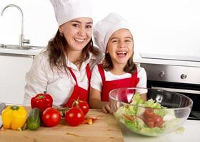 Mujer e hija preparando ensalada en la cocina de casa foto