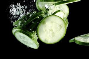 Cucumber slices falling into water at black background