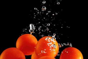 Cherry tomatoes falling into water at black background