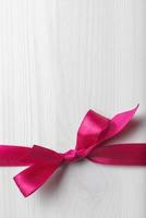 Pink ribbon and bow against white wooden background