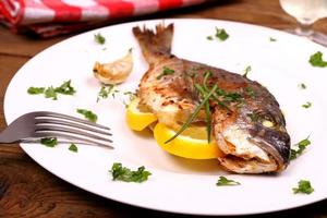 Grilled sea bream fish, lemon on white plate