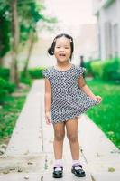 Feliz niña asiática en vestido de pie en la acera en el parque foto