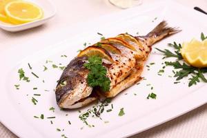 Grilled sea bream fish, lemon, arugula on white plate