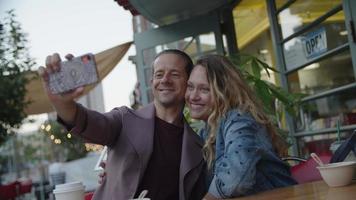 câmera lenta de casal tirando selfie na calçada da cafeteria