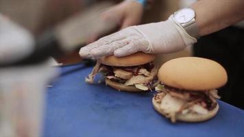 kook in handschoenen, bedek gekookte hamburger voor broodje. Fast food. zonnige zomerdag. openlucht evenement