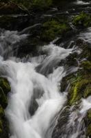Cascade of small waterfall over mossy rocks, long exposure.